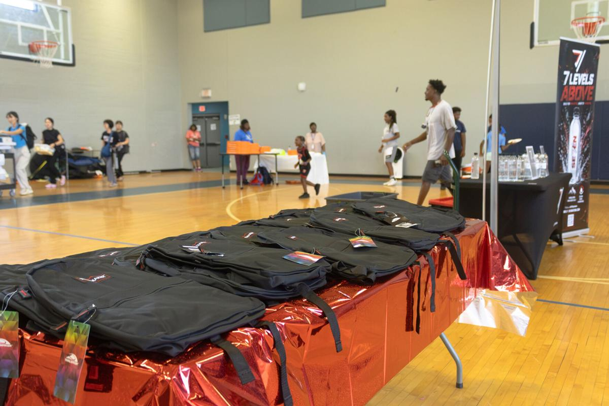 Rows of black backpacks laid out on a table at a back to school giveaway in a gym